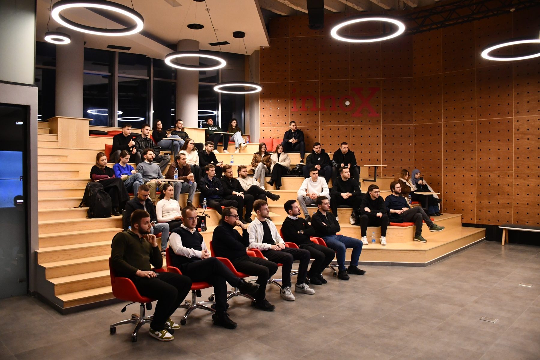 Young people and guests seated on the wooden tiered steps at InnoX Center during a HEY event